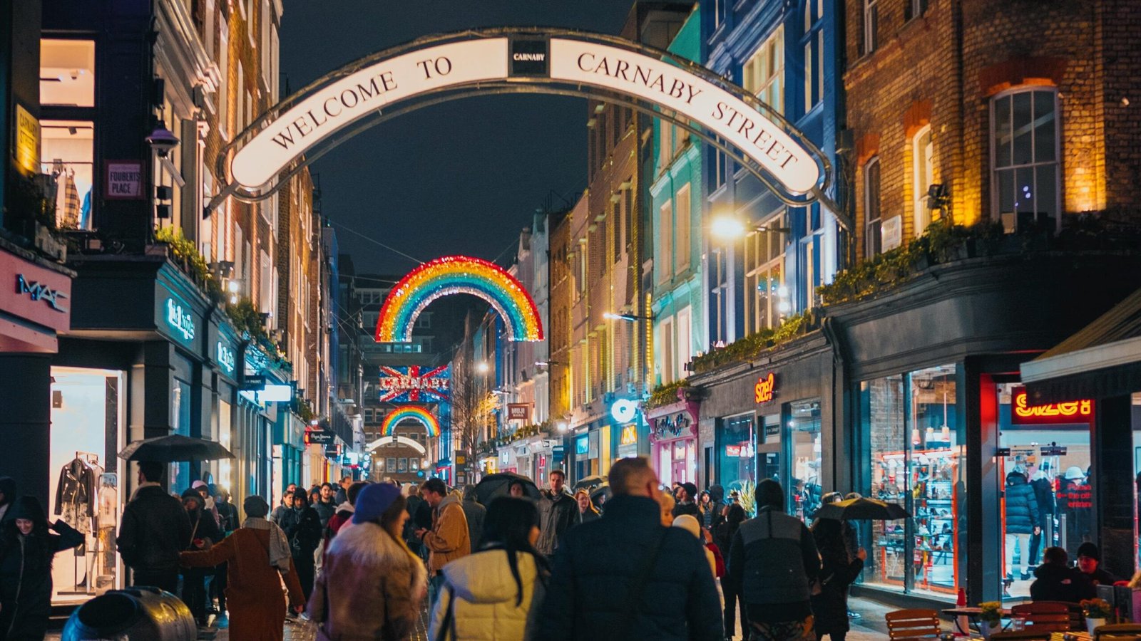 A bustling night scene on Carnaby Street, London, with people walking under colorful neon lights.